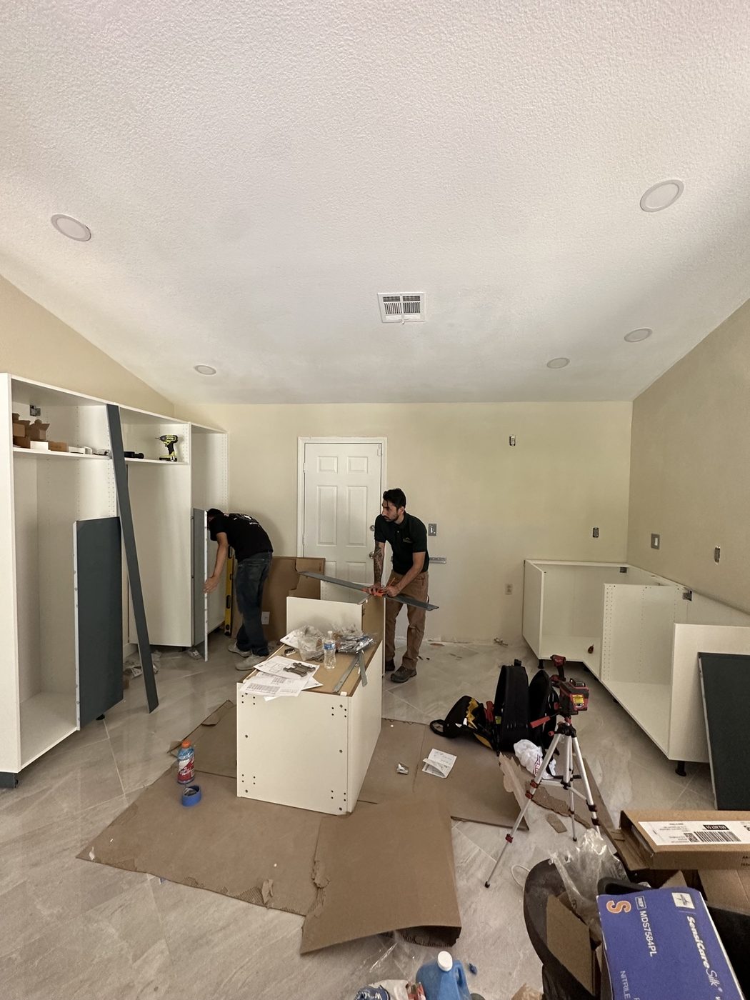 Two technicians assembling white base cabinets during a kitchen install